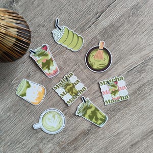 May include: A collection of matcha-themed stickers featuring various matcha drinks, including a latte with latte art, a matcha latte with a strawberry, and a matcha drink with whipped cream. The stickers also include a bowl of matcha and a matcha whisk.