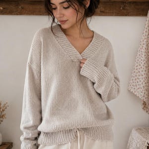 Può includere: Un maglione beige con scollo a V caratterizzato da una trama a maglia grossa, maniche lunghe con polsini a coste e un orlo a coste. Il capo è realizzato in un filato morbido dai toniido dai toni neutri e presenta una vestibilità ampia e rilassata.