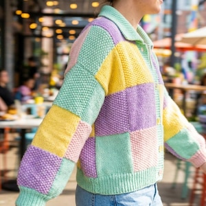 May include: A colorful patchwork cardigan in pastel shades of yellow, pink, green, and purple. The knitted sweater features a collared neckline and button-down front. The sleeves and body are composed of various rectangular blocks of color.