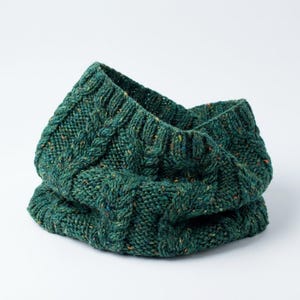 Könnte beinhalten: Ein grüner Strickschal mit Zopfmuster. Der Schal ist aus einem dicken, strukturierten Garn mit Farbtupfern gefertigt. Der Schal ist gefaltet und zeigt die Innenseite.