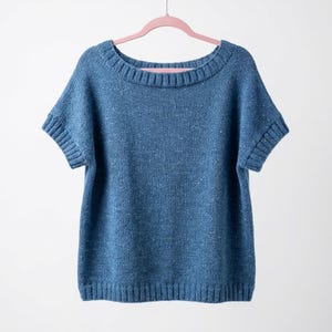 May include: A short-sleeved knit sweater in a medium blue color with subtle white flecks throughout the fabric. The garment features a wide, rounded neckline and ribbed trim along the collar, sleeve cuffs, and the bottom hem of the sweater.