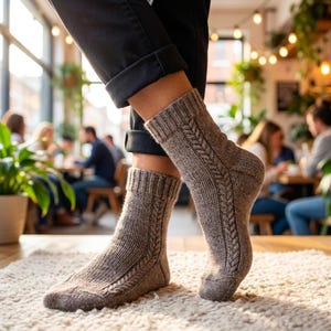 May include: A close-up of brown knitted socks featuring a cable knit pattern. The socks are worn with black trousers. The background shows a cafe setting with people seated at tables, and a white rug.