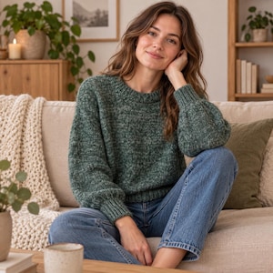 Könnte beinhalten: Ein waldgrüner, melierter Strickpullover mit Rundhalsausschnitt und langen, leicht bauschigen Ärmeln mit gerippten Bündchen und Saum. Der Pullover wird mit einer klassischen blauen Jeans kombiniert, was ein lässiges und bequemes Outfit ergibt.