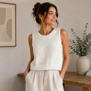 May include: A sleeveless white knit sweater vest featuring a ribbed crew neckline and a ribbed hem. The garment is crafted from a soft, textured yarn with a slightly cropped length, providing a clean and simple look for any wardrobe collection.