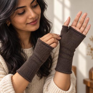 Könnte beinhalten: Ein Paar dunkelbraune fingerlose Handschuhe mit gerippter Strickstruktur. Die Handschuhe reichen von den Knöcheln bis zur Mitte des Unterarms und haben einen einfachen Rollsaum an den Öffnungen sowie eine Öffnung für den Daumen.