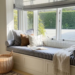 May include: A window seat with blue and white striped cushions and pillows. A brown pillow and a white pillow with an anchor design are also present. A woven basket and a blanket are visible. An open book rests on the seat.