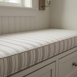 May include: A rectangular bench cushion with a cream background and vertical stripes in red and navy blue. The cushion has a white border and is on a grey bench with two drawers.