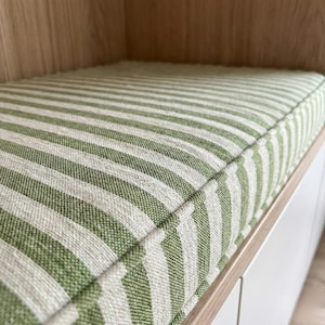 May include: A rectangular bench cushion featuring a green and white striped design. The cushion is made of a textured fabric and is set within a wooden frame. The stripes run vertically.