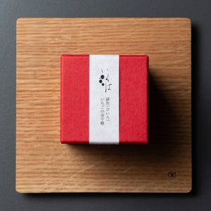 May include: A red square box with a white band and Japanese text, on a wooden square. The box has a textured surface. The wooden square has a natural wood grain.