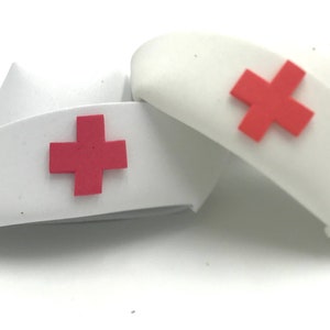 May include: Two white nurse hats with red crosses. The hats are made of a soft, pliable material and are perfect for a costume or play.