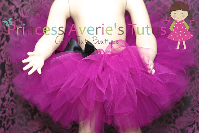 May include: A fuchsia tulle tutu with a black satin bow. The tutu is worn by a child mannequin. The text "Princess Averie's Tutus" is visible in the image.