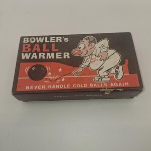 May include: A rectangular cardboard box for a Bowler's Ball Warmer. The box is dark brown with red accents and features a cartoon illustration of a person bowling. Text on the box reads: BOWLER'S BALL WARMER, HOT SHOTS, and NEVER HANDLE COLD BALLS AGAIN.