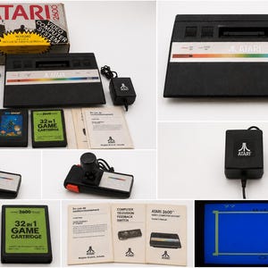 Puede incluir: Una consola de videojuegos Atari 2600 negra con una franja arcoíris, dos joysticks negros con botones rojos, un adaptador de corriente, dos cartuchos de juego etiquetados Sea Ghost y 32 in 1, manuales impresos y la caja de cartón original.