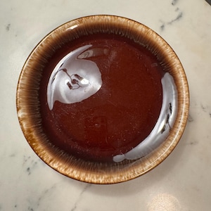 May include: A brown and white glazed ceramic plate with a rim. The plate has a brown center and a white rim with brown streaks.
