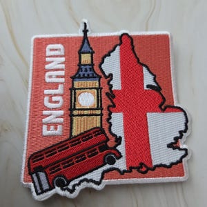 Op de afbeelding: Geborduurde patch met Engelse symbolen. Het toont een rode dubbeldekkerbus, Big Ben en een kaart van Engeland met een rood kruis. Het woord "ENGLAND" staat in witte blokletters op een rode achtergrond.