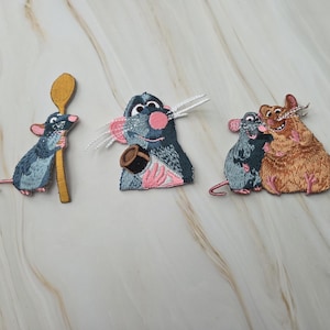 Op de afbeelding: Drie geborduurde patches met tekenfilmratten. De eerste is een grijze rat die een gele houten lepel vasthoudt. De tweede is een grijze rat met een kleine bruine pot. De derde is een grijze rat naast een grotere, lichtbruine rat.