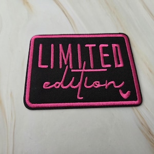 Op de afbeelding: Een rechthoekige geborduurde patch met een zwarte achtergrond en een felroze rand. De tekst LIMITED is in roze blokletters geborduurd boven het woord edition in een roze cursief schrift, met een klein roze hartje aan het einde van de tekst.