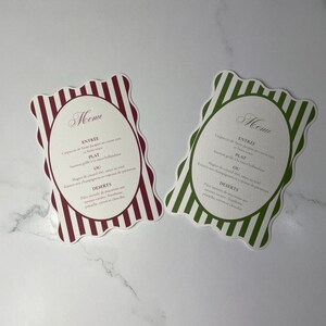 Peut inclure: Deux cartes de menu aux bords festonnés. L'une a une bordure rayée bordeaux et blanche, l'autre une bordure rayée verte et blanche. Chaque carte a un centre ovale avec le mot "Menu" en haut et des plats de menu en dessous.