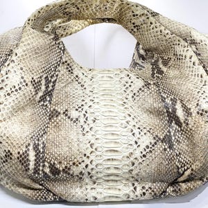 May include: A large, beige and brown snakeskin handbag with a single handle. The bag has a rounded shape and a textured surface, showcasing the natural pattern of the snakeskin. The neutral color palette makes it a versatile accessory.
