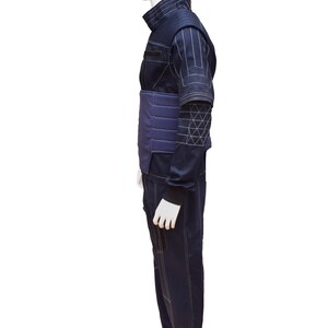 May include: A dark blue jumpsuit with white stitching and a padded waist belt. The jumpsuit has a high collar and long sleeves.