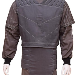 May include: A grey padded vest with a V-shaped design and a high collar. The vest has a quilted texture and is worn over a long-sleeved shirt with a striped pattern.