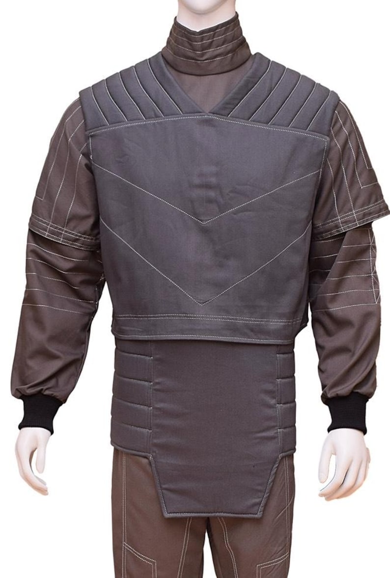 May include: A grey padded vest with a V-shaped design and a high collar. The vest has a quilted texture and is worn over a long-sleeved shirt with a striped pattern.