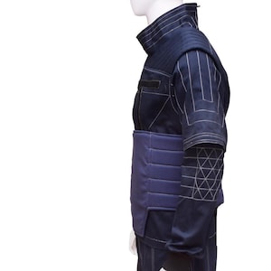 May include: A dark blue jacket with a padded, quilted chest and a geometric pattern on the sleeve. The jacket has a high collar and a zipper closure.