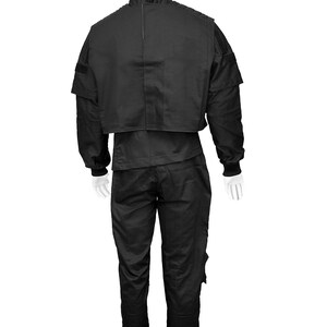 May include: A black tactical jumpsuit with a zip-up jacket and pants. The jacket has a high collar and a patch on the shoulder. The pants have multiple pockets.