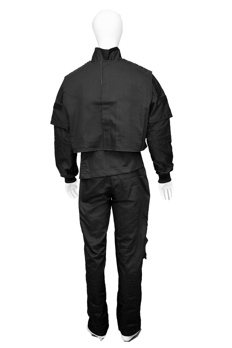 May include: A black tactical jumpsuit with a zip-up jacket and pants. The jacket has a high collar and a patch on the shoulder. The pants have multiple pockets.