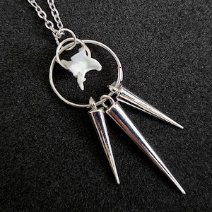 May include: A silver-toned necklace featuring a delicate chain attached to a circular metal ring. Suspended from the ring are three polished silver-toned metal spikes and a small, white, textured bone-like element centered within the circle.