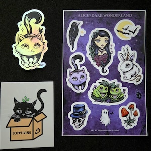 May include: A collection of stickers including a holographic cat, a black cat in a cardboard box labeled ECO LIVING, and a rectangular sheet titled ALICE'S DARK WONDERLAND featuring illustrations of a raven, a girl, bats, a rabbit, frogs, a skull, a ghost, and mushrooms.