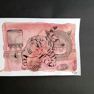 May include: A black and white line drawing of a cat looking at two fish on a pink watercolor background. The cat is near a wicker basket and a small wooden stool.