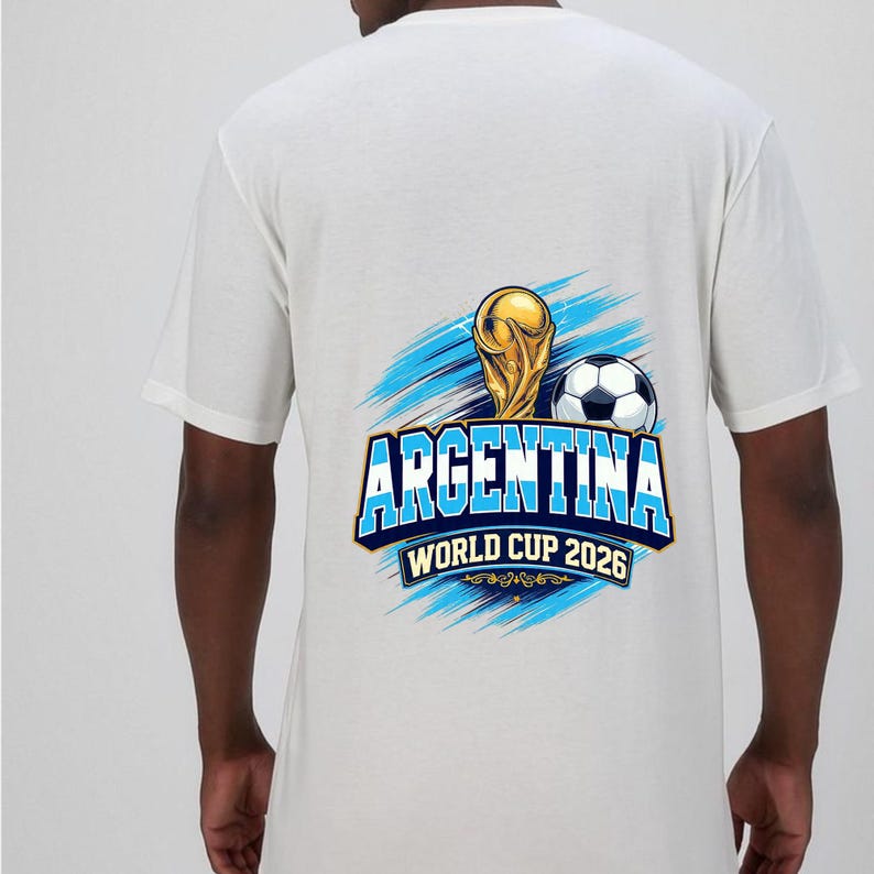 May include: White t-shirt featuring a graphic design for Argentina's World Cup 2026. The design includes a gold trophy, a soccer ball, and the word "ARGENTINA" in blue and white, with the text "WORLD CUP 2026" below.