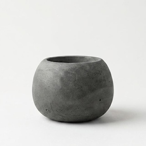 Op de afbeelding: Een kleine, ronde, grijze betonnen plantenbak met een brede opening. De plantenbak heeft een gladde, matte afwerking en een eenvoudig, modern ontwerp. Perfect voor kleine planten of vetplanten.
