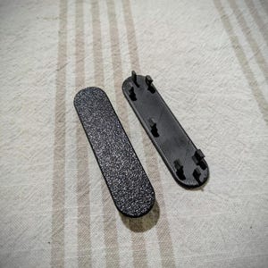 May include: Two black plastic pieces with a textured surface and multiple small prongs on one side.