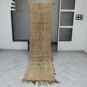 May include: A long, rectangular rug with a brown and beige background. The rug features a geometric pattern in shades of blue, pink, and white. The rug has a fringe on the bottom.