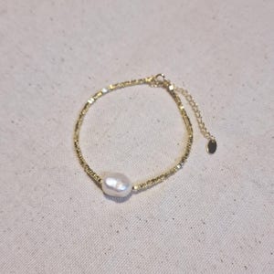 May include: A delicate gold chain bracelet with a single large white pearl charm. The bracelet has a small extension chain for adjusting the fit.