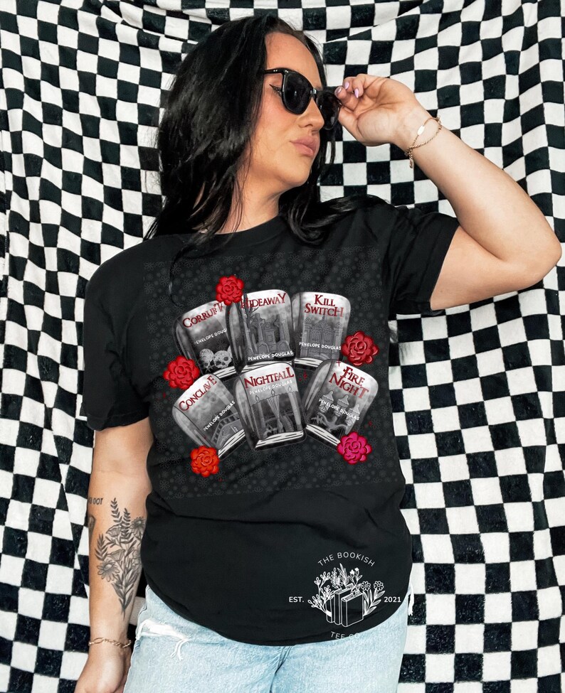 May include: Black t-shirt featuring a graphic of book covers with titles like "Corrupt" and "Nightfall," surrounded by red roses. The text "THE BOOKISH TEE" and the year 2021 are printed at the bottom. The shirt is a casual wear item.