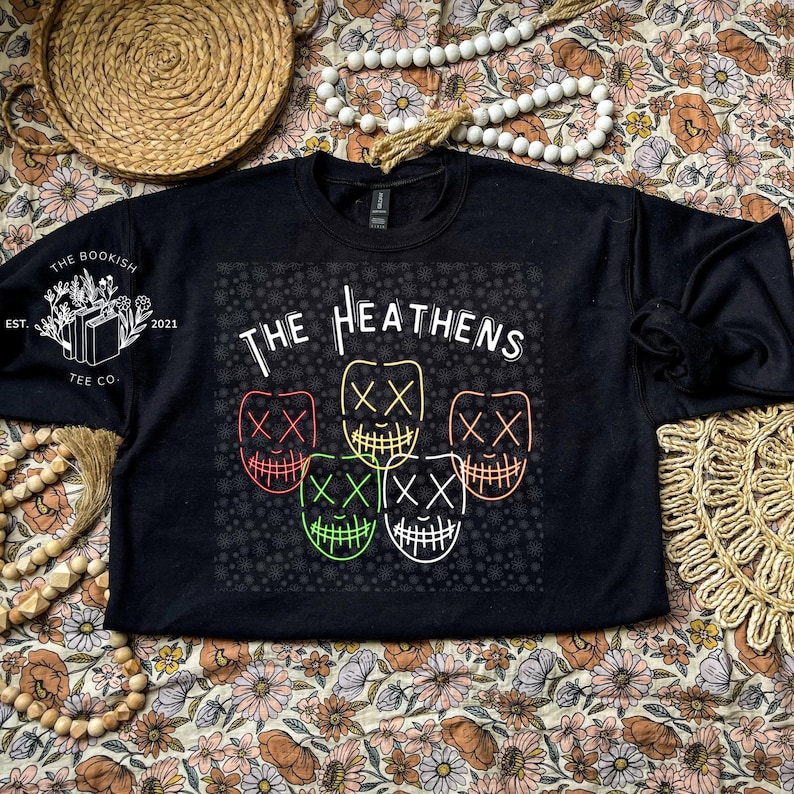 Może przedstawiać: Czarna bluza z białym nadrukiem graficznym z tekstem "The Heathens" i pięcioma stylizowanymi twarzami z oznaczeniami "XX". Grafika jest otoczona wzorem małych białych kropek.