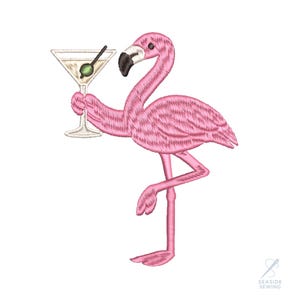 May include: Embroidered pink flamingo holding a martini glass with an olive. The flamingo has a black beak and is standing on one leg. The martini glass is clear with a green olive and a black cocktail stick.