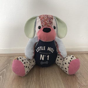 May include: A plush patchwork dog toy with a pink nose and green ears. The dog is wearing a blue shirt with the text "Little Miss Adorable No. 1" on it.