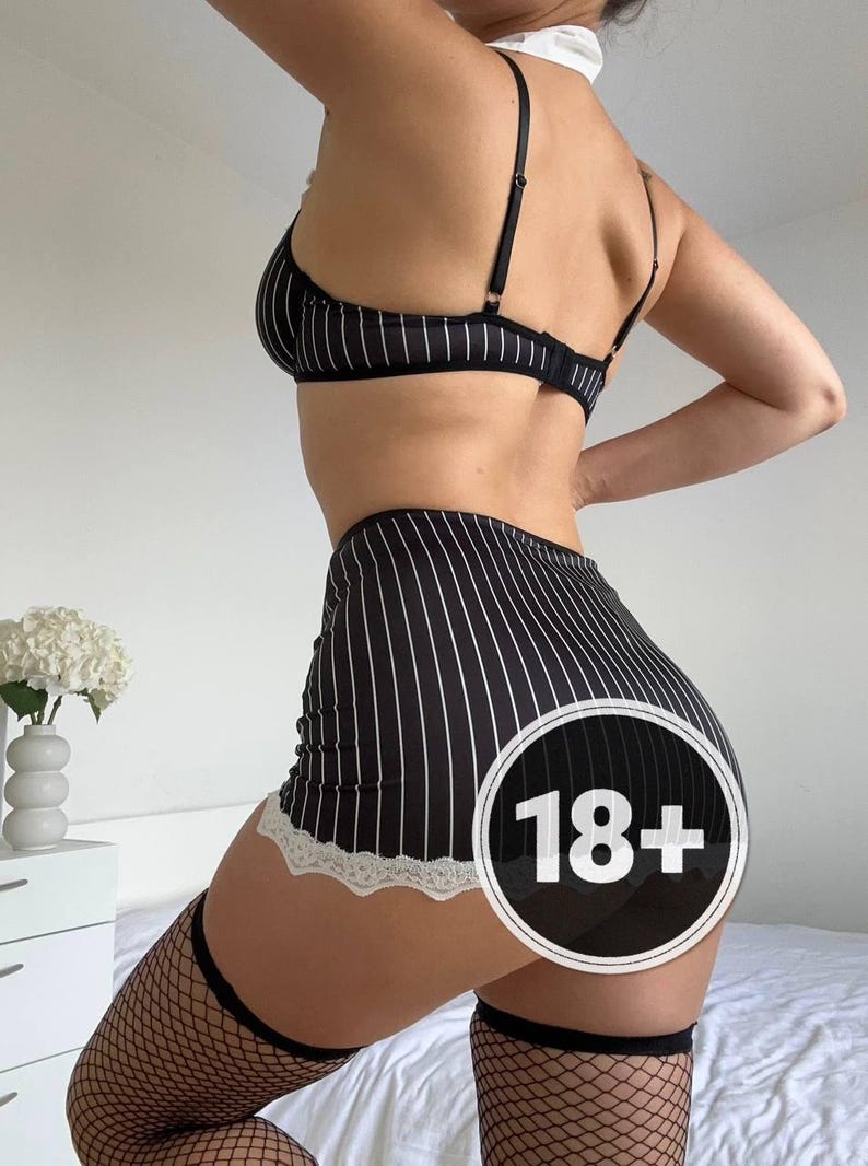 May include: Black and white striped lingerie set, including a bra and high-waisted skirt with lace trim. The outfit is paired with fishnet stockings. A white collar is also visible.
