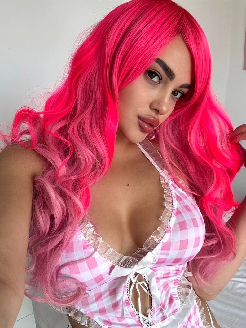 May include: A woman with long, wavy, bright pink hair and a pink and white gingham patterned top. The top has a lace trim and a tie-up front. The hair has a gradient effect, transitioning to a lighter pink at the ends.