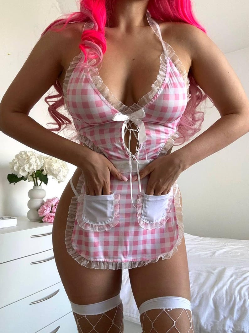 May include: A pink and white gingham lingerie set with a halter top and apron-style skirt. The top features a lace trim and a bow detail at the bust. The apron has two pockets and a ruffled edge. The set is designed with a playful and feminine aesthetic.