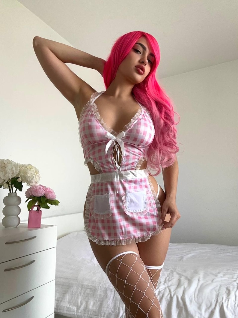 May include: Pink and white gingham lingerie set with a matching apron. The top has a halter neck and a bow detail. The apron has two pockets and a ruffled edge. The model is wearing white fishnet stockings.