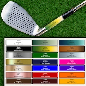 May include: A golf club iron with a silver head and black grip, set against a green background. The image includes a selection of customizable name tags in various colors, each with fields for name, address, and phone number.