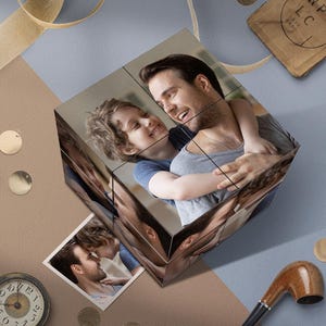 Pode incluir: Um cubo de fotos personalizado com um homem e uma criança sorrindo. O cubo é composto por várias imagens, mostrando um abraço amoroso. O fundo inclui um relógio, um cachimbo e elementos decorativos.