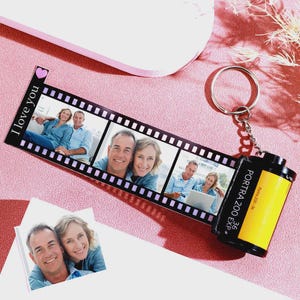 Op de afbeelding: Een gepersonaliseerde filmstrip sleutelhanger met een fotocollage. De zwarte filmstrip heeft de woorden "I love you" en een roze hart. De sleutelhanger bevat een gele en zwarte filmcassette met de tekst "PORTRA 200 EXP".