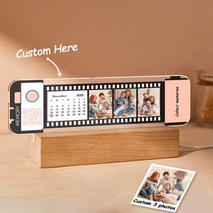 May include: A custom photo display in a film strip design, with family photos, a December 2022 calendar, and the word "MEMORY". It is mounted on a wooden base and includes a small photo with the text "Custom 3 photos".