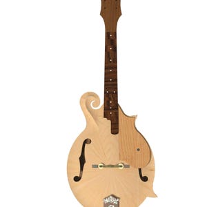 May include: A mandolin with a light-coloured wooden body featuring a sunburst grain pattern, a dark wooden neck, and a scroll-shaped headstock. It includes an f-hole, a bridge, a tailpiece with decorative metal engraving, and a wooden pickguard.